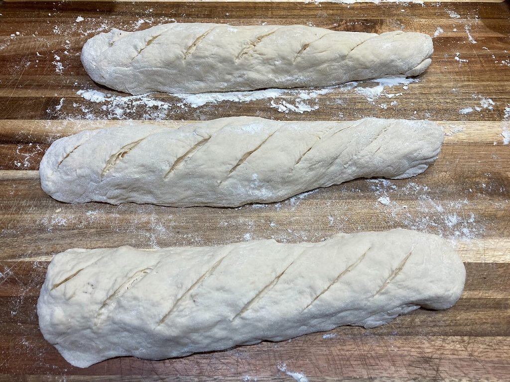 Tres baguettes de masa cruda con harina sobre una tabla