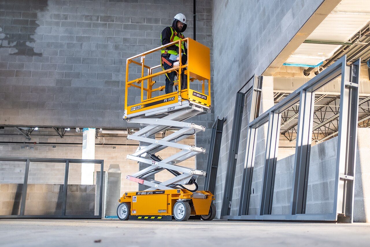Operario trabajando en una plataforma de tijera elevada en el interior de un edificio