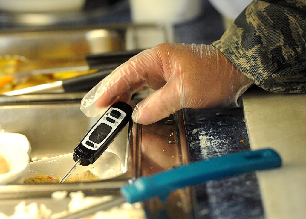 Manipulador con guante midiendo la temperatura de un alimento con termómetro